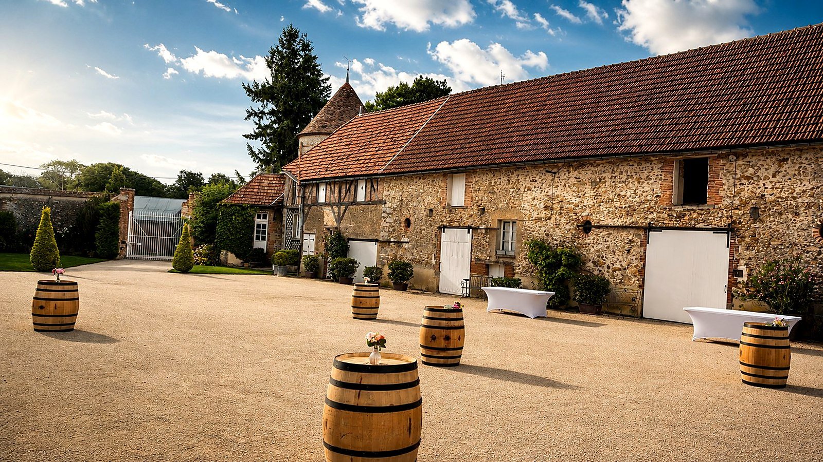 Vin d'honneur de mariage en extérieur avec tonneaux en bois et mange-debout, devant une bâtisse en pierre, mise en place BLK Production pour réception champêtre